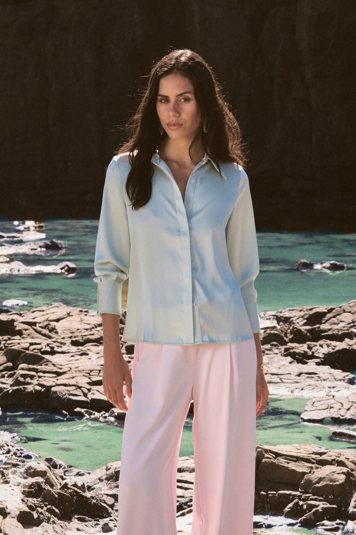Mae Satin Shirt in mint worn front on with pink wide-leg trousers, coastal rocks behind