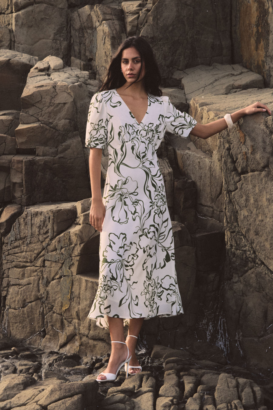 Natalie V-Neck Floral Dress in cream and olive floral print, worn standing on rocks
