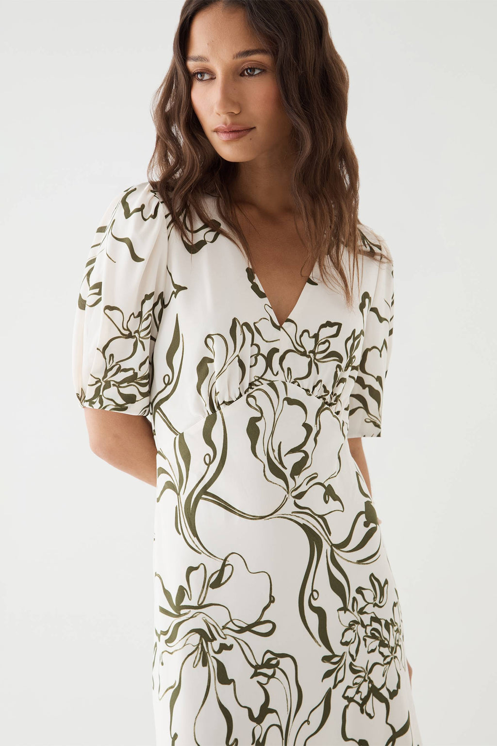 Close-up of the deep V-neckline and olive botanical print on the cream dress