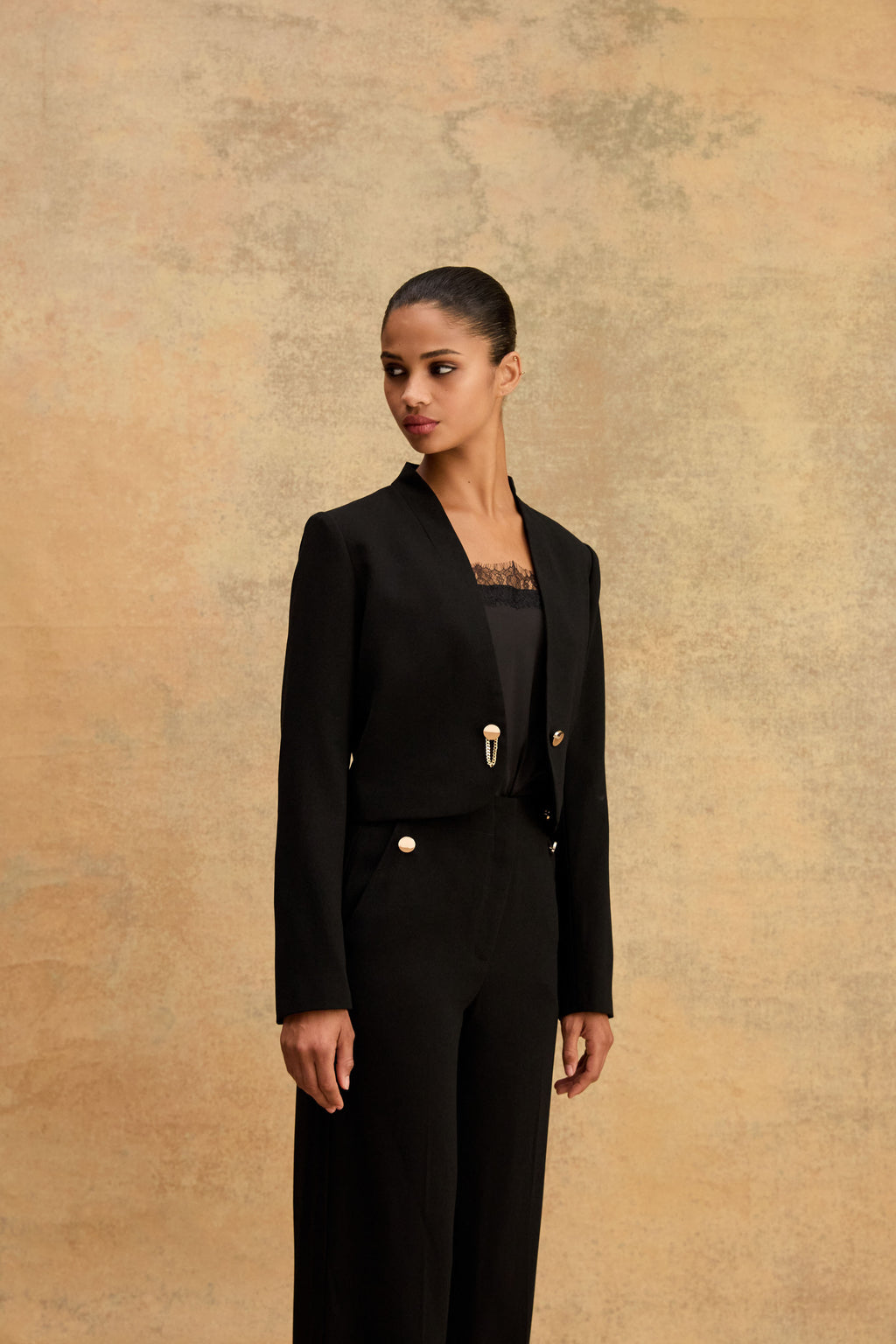Side view of the black cropped jacket showing gold-tone clasp and curved hemline