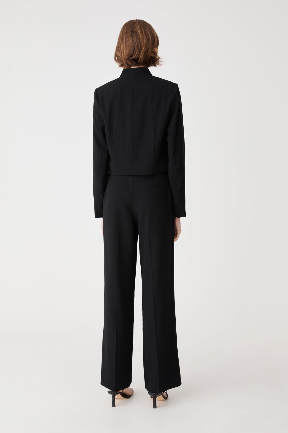 Back view showing centre-back seam and vertical darts of the black cropped jacket