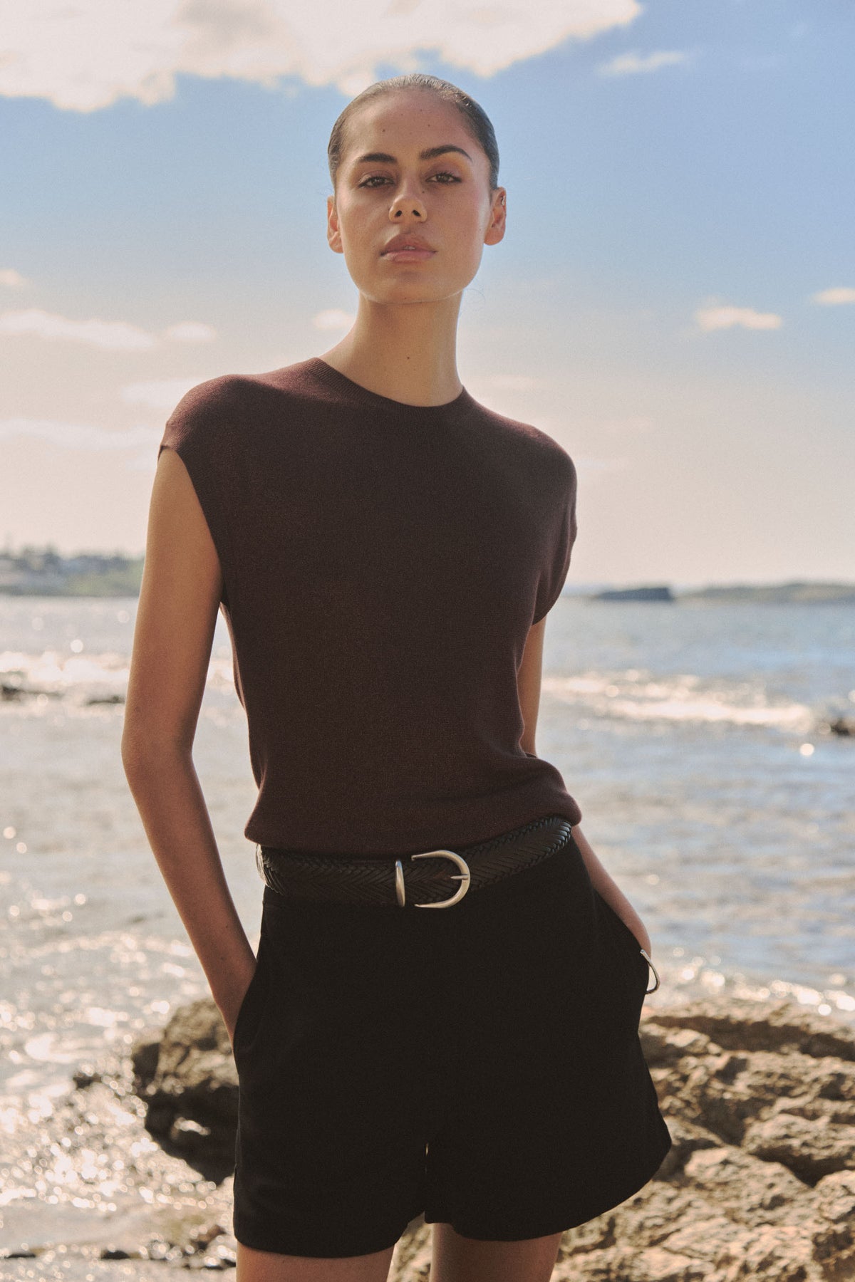 Saskia Lurex Knit Top in Fudge worn with black shorts and belt, outdoor coastal setting, front view