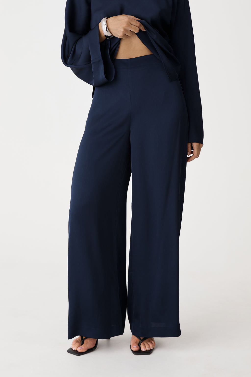 Close-up of the navy satin pants' fixed waist and wide-leg drape, front view