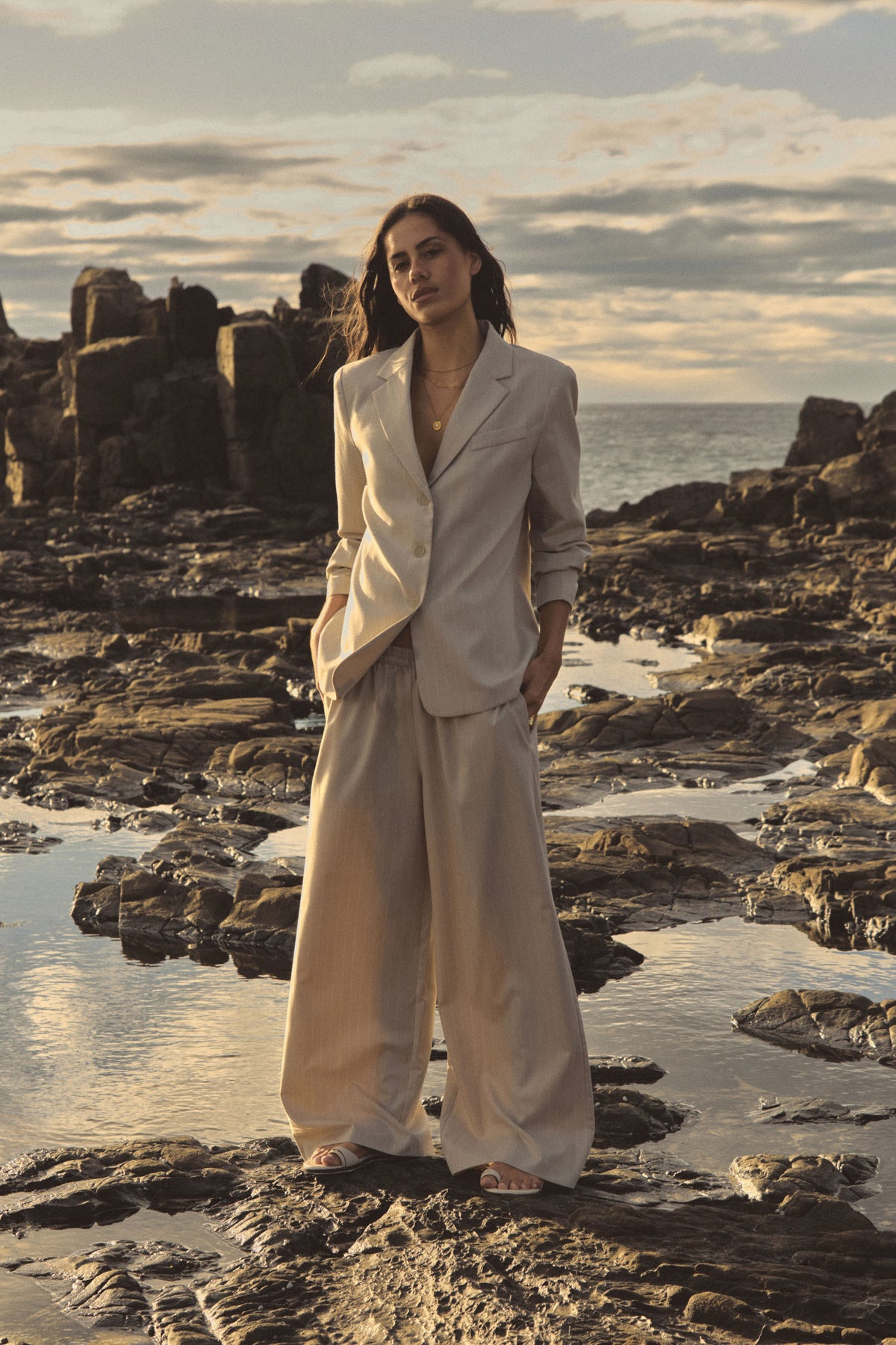 Zoe Elastic Pinstripe Pants in beige pinstripe worn on rocks with a matching blazer, full-length front view