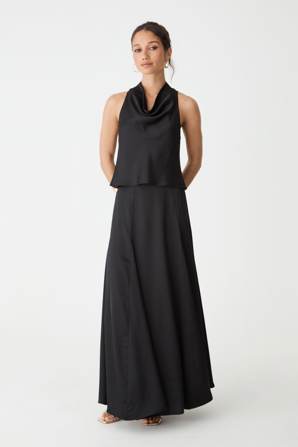 Freya Satin Cowl Top in black, front view, sleeveless with draped cowl neckline, worn with a long black skirt