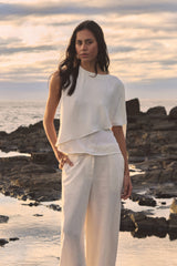 Cecilia Asymmetric Top in ivory worn with ivory wide-leg trousers, front view outdoors by the sea