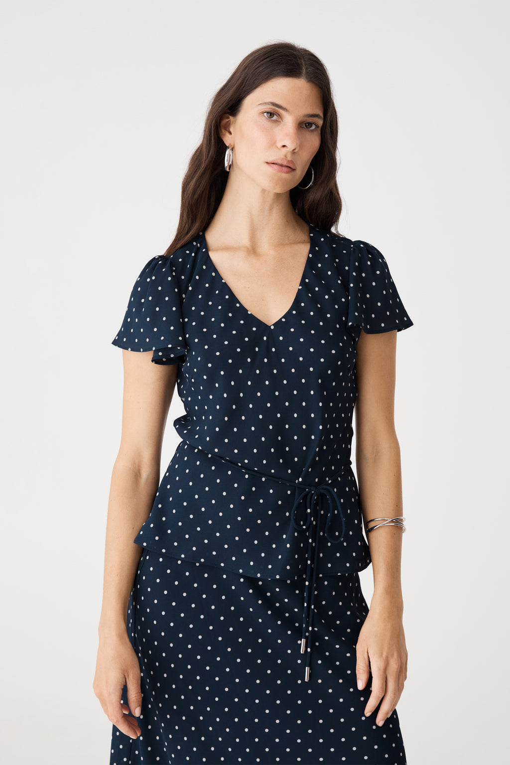 Close-up front view of the V-neckline, white polka dot print and short frill sleeves