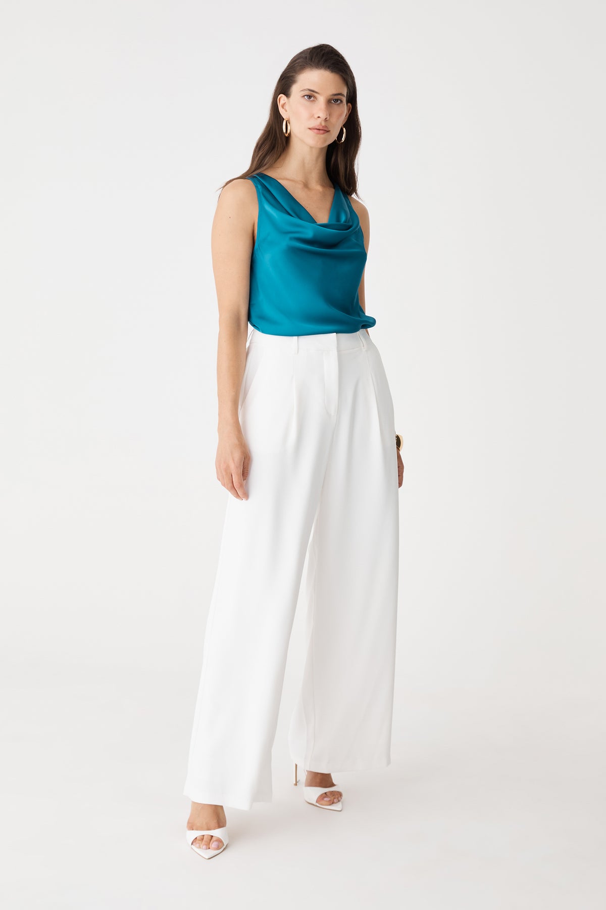 Front view of the aquamarine Aurelia Satin Cowl Neck Top worn with white wide-leg trousers